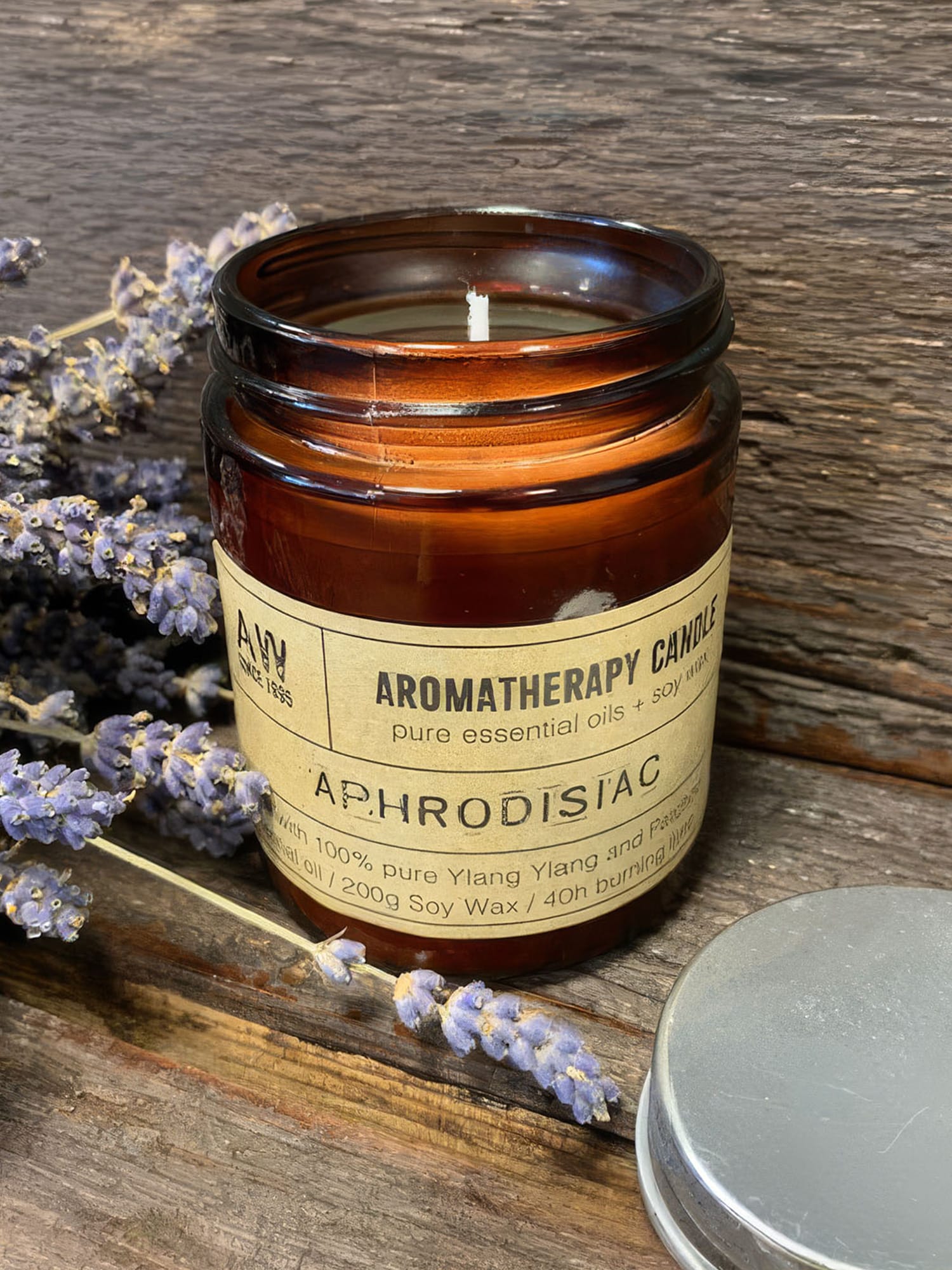 Unlit amber Aphrodisiac candle jar on rustic wood with lavender sprigs and silver lid off.