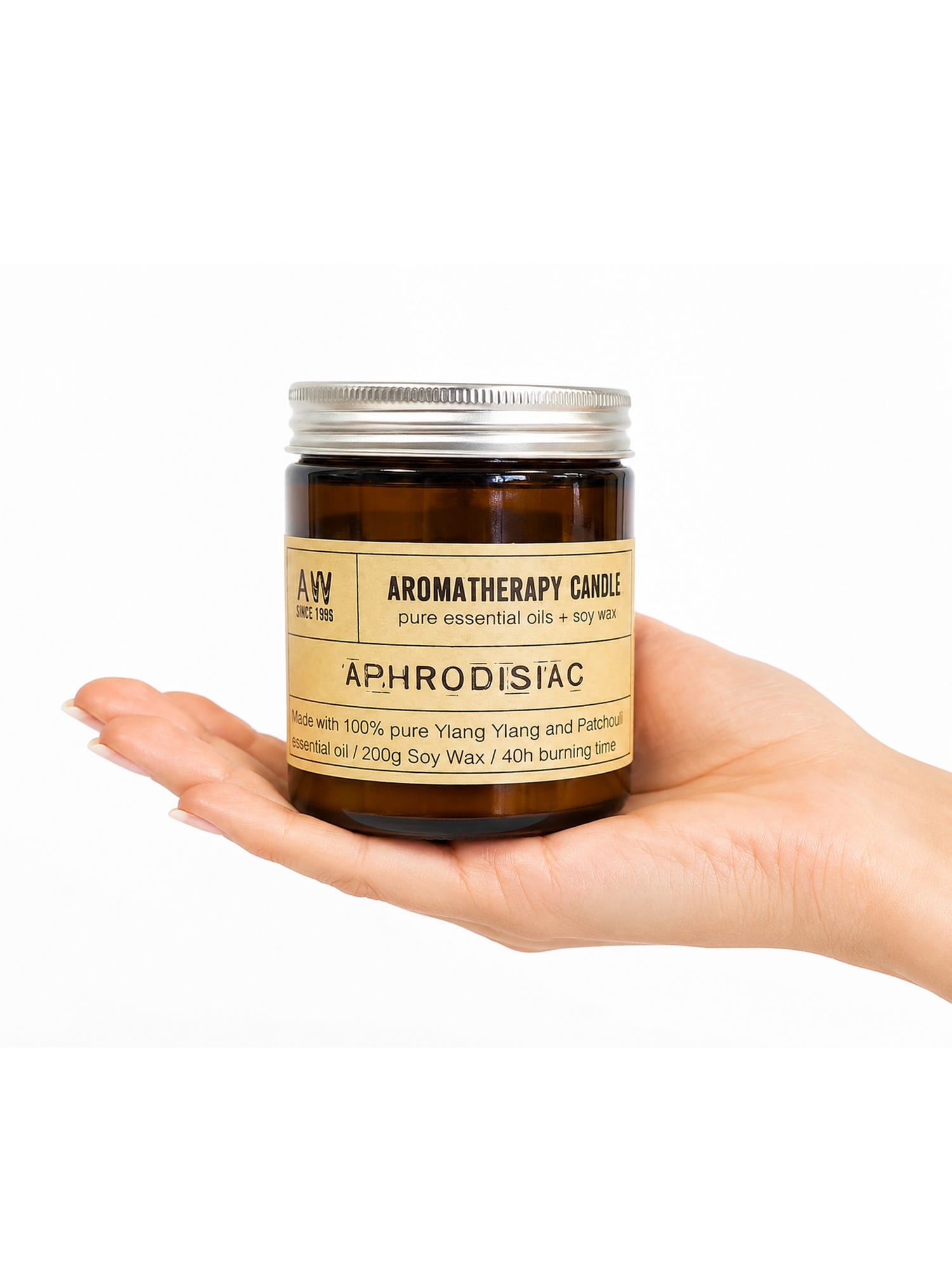Hand holds amber Aphrodisiac Ylang Ylang candle jar with cream label and silver lid.