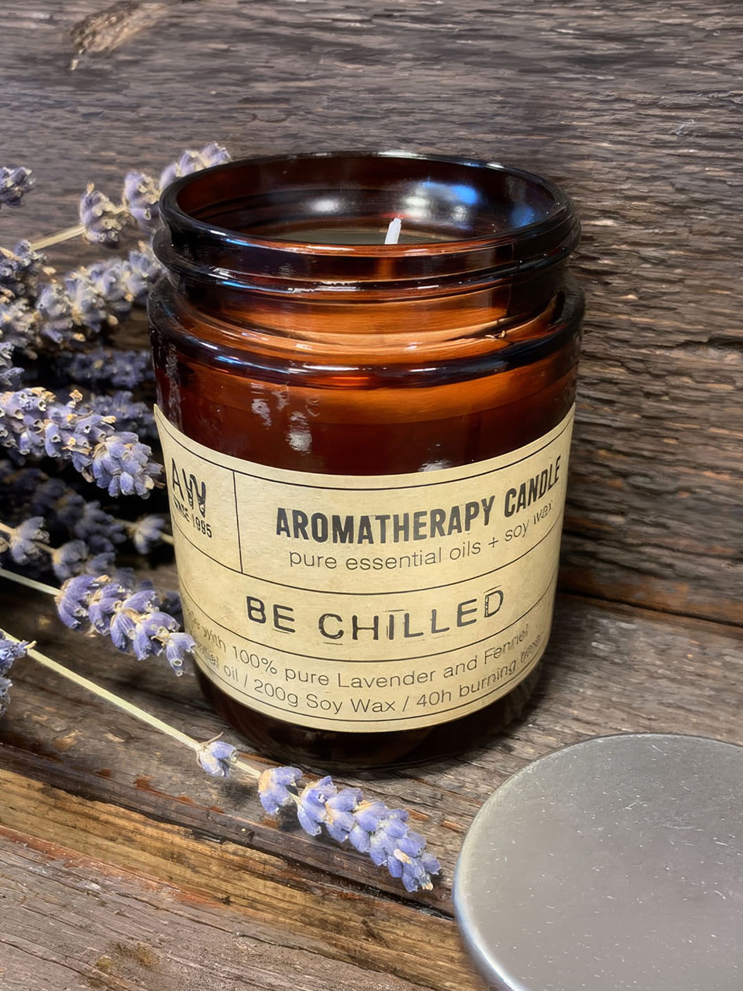 Unlit amber Be Chilled candle jar on rustic wood with sprigs of lavender and lid off.