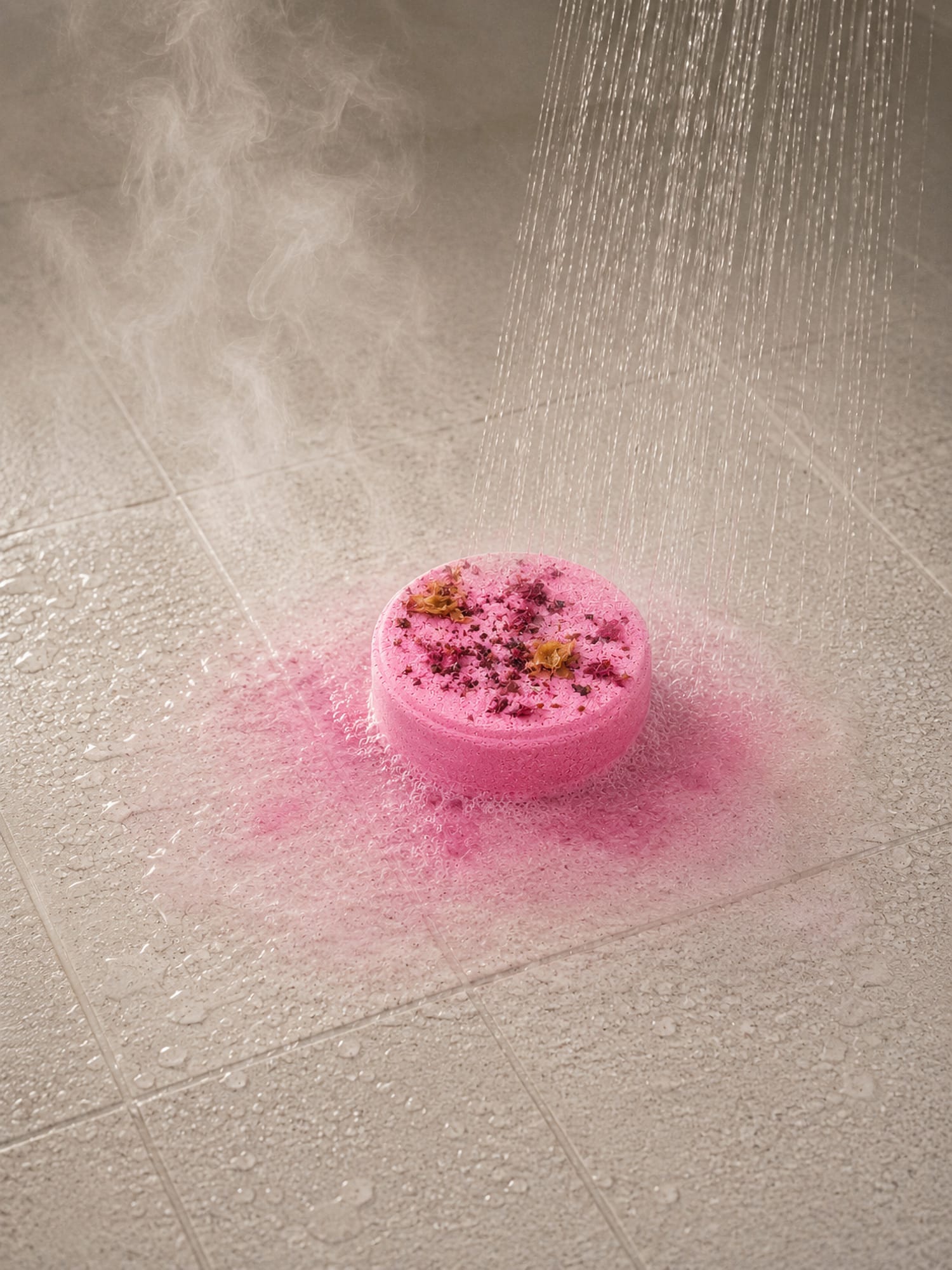 Pink Love Potion shower steamer dissolving under shower spray on wet tiles.