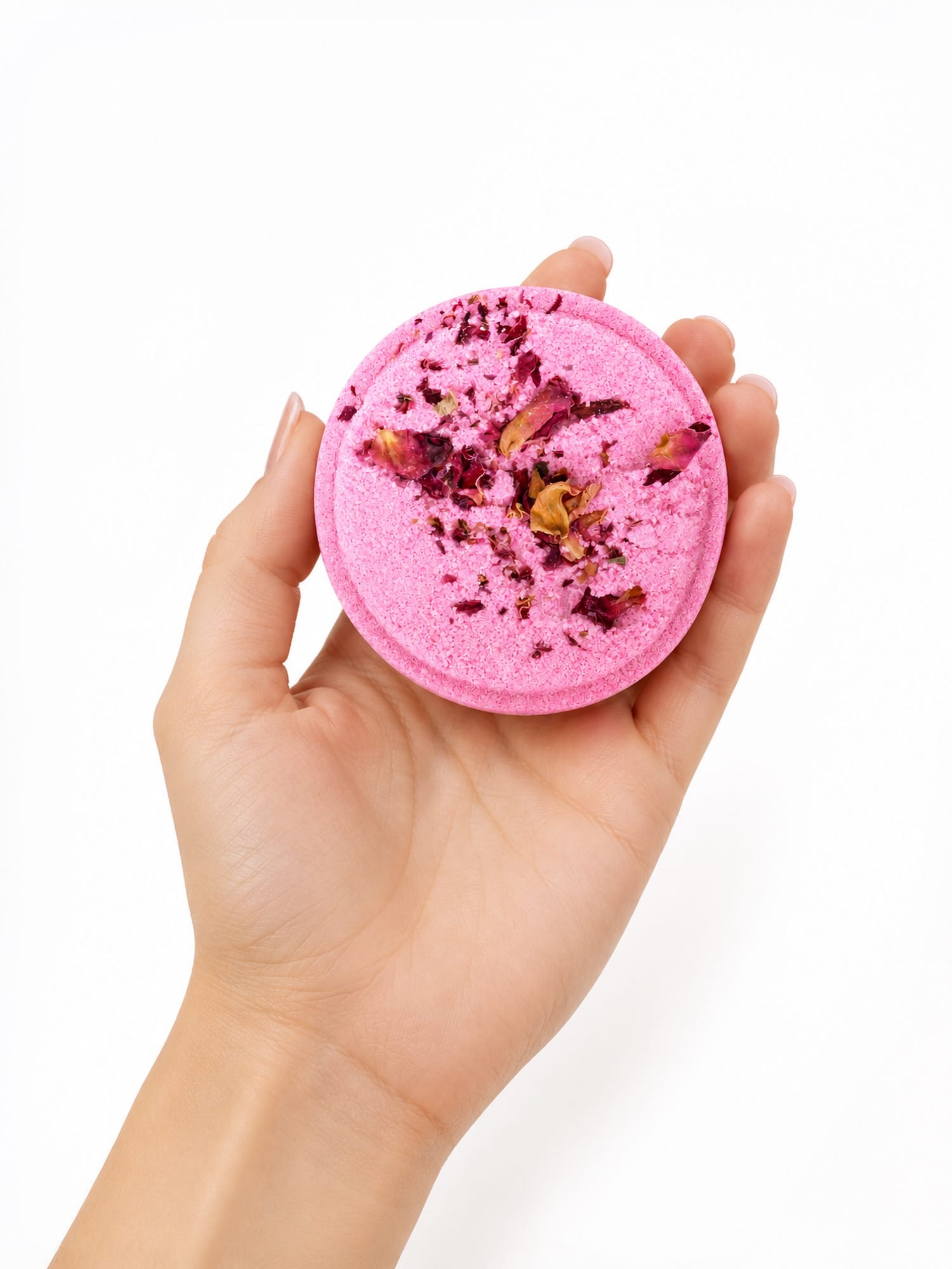 Hand holding round pink Love Potion shower steamer with dried petals on white background.