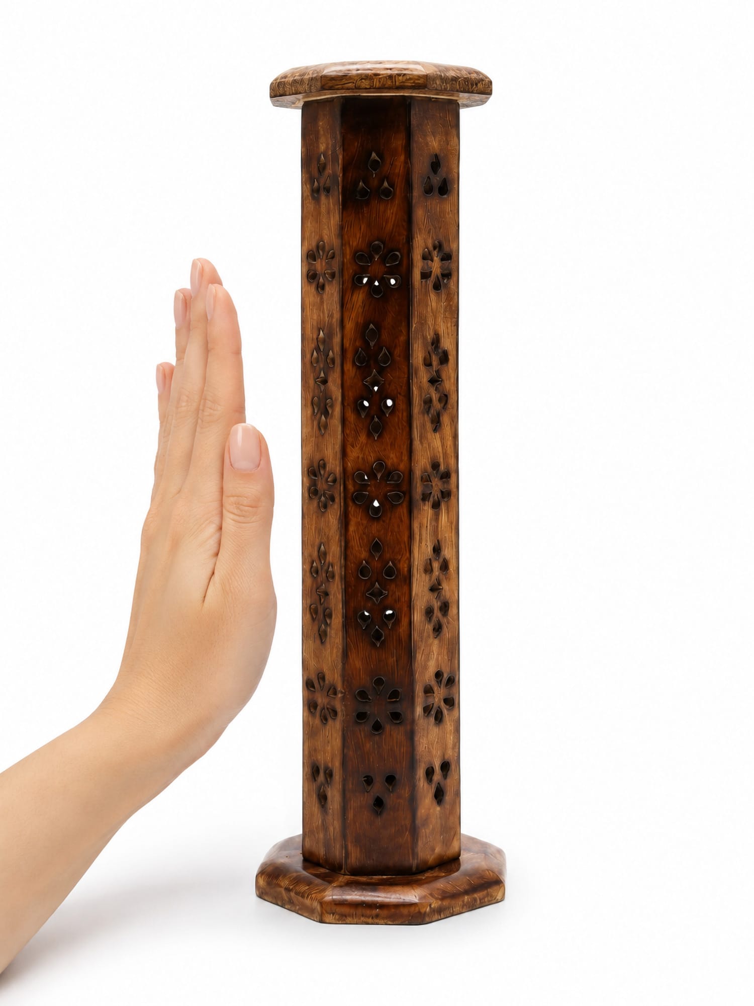 Hand beside hexagonal mango wood incense tower with floral cut‑outs, showing its height.