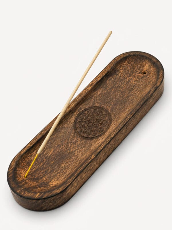 Mandala carved mango wood incense tray with incense stick resting on long oval dish.