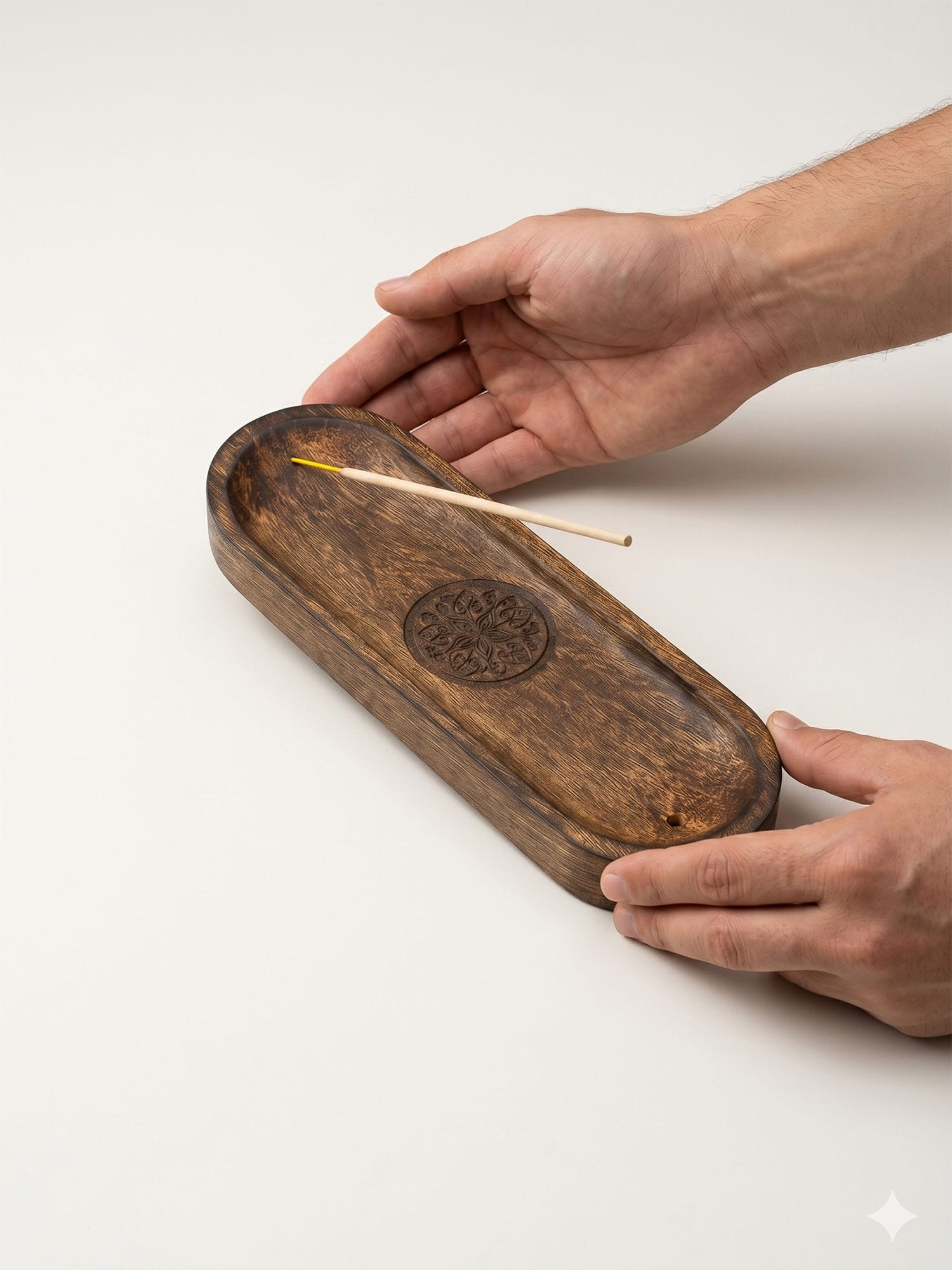 Hands holding long mango wood incense tray with carved mandala and incense stick for scale.