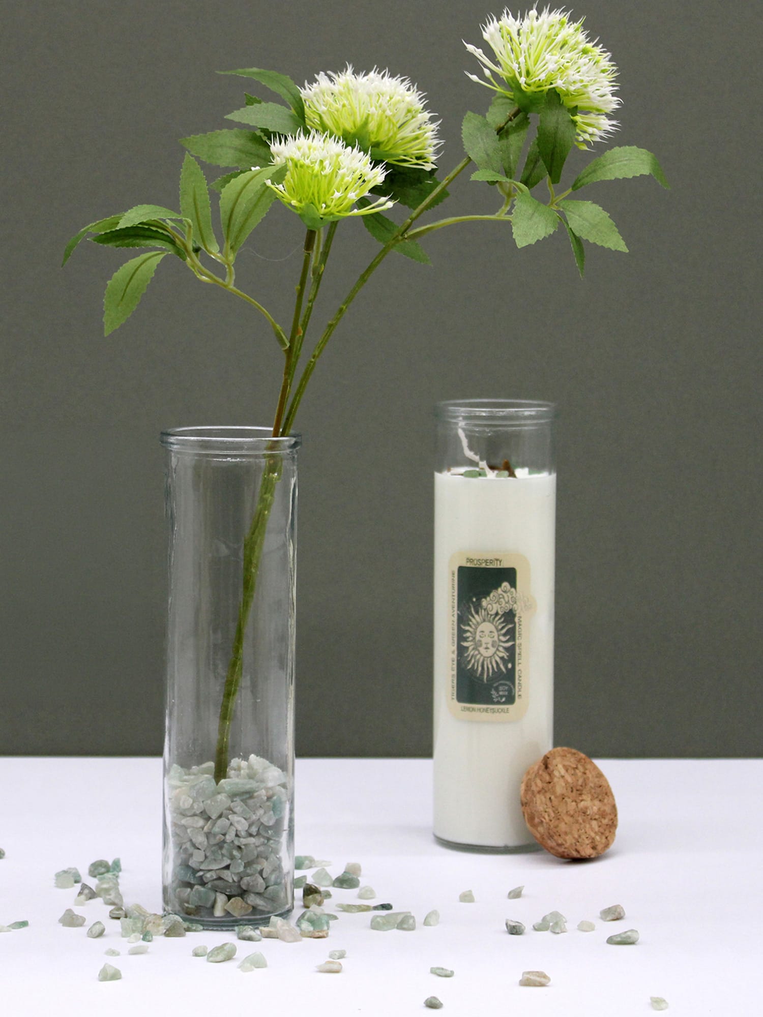 Seduction & Passion Gemstone Ritual Candle with green pompom flowers and scattered pale stones.