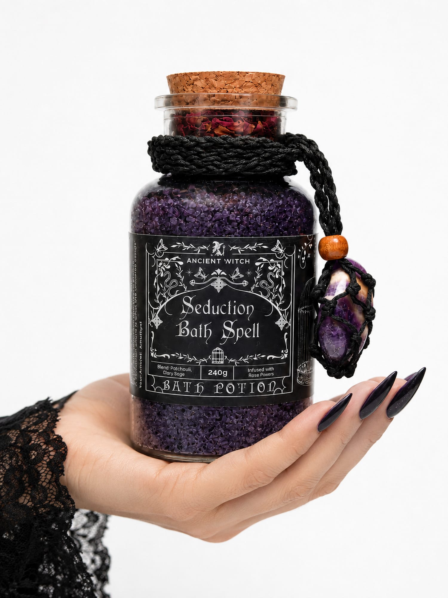 Hand with long nails holding Seduction Bath Ritual jar with dark purple salts and amethyst amulet.