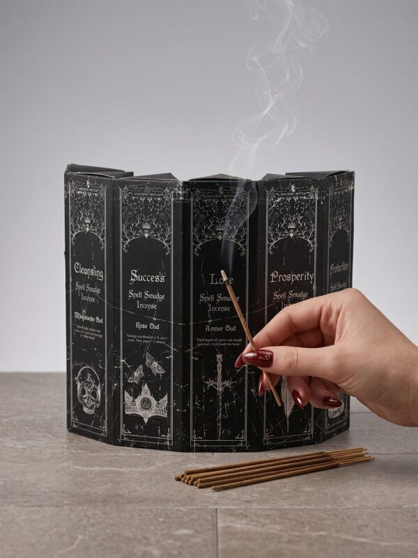 Open multi-intention incense box with panels of different intentions and a hand lighting a stick.