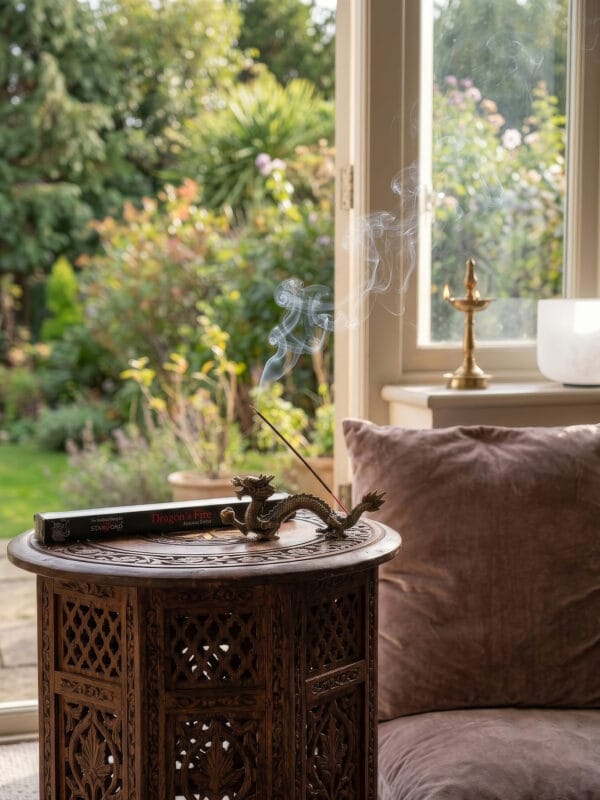 Dragon's Fire incense burning in dragon holder on carved table by open doors and green garden.