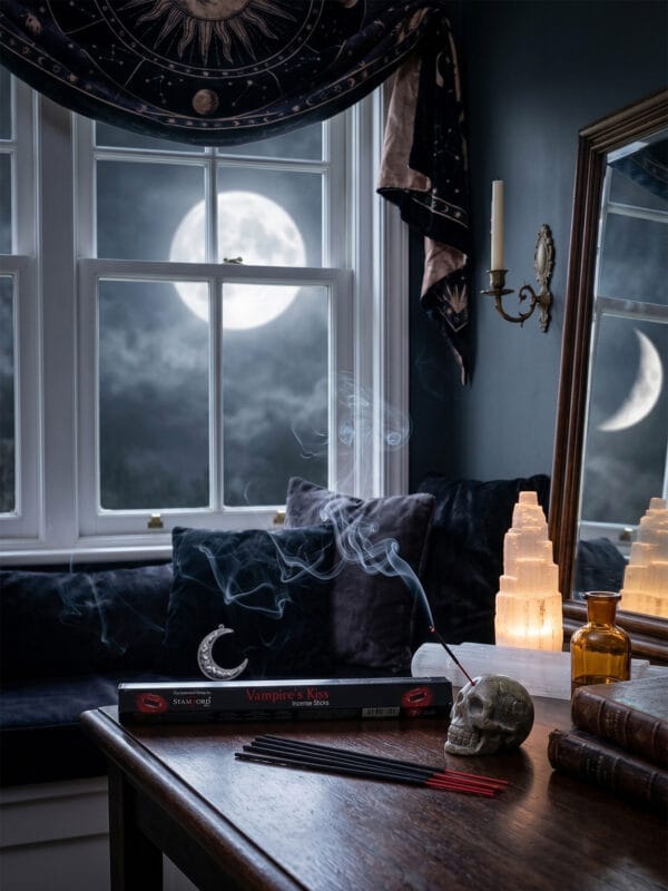 Vampire's Kiss incense burning in skull holder on table with full moon view, red sticks and crescent ornament.