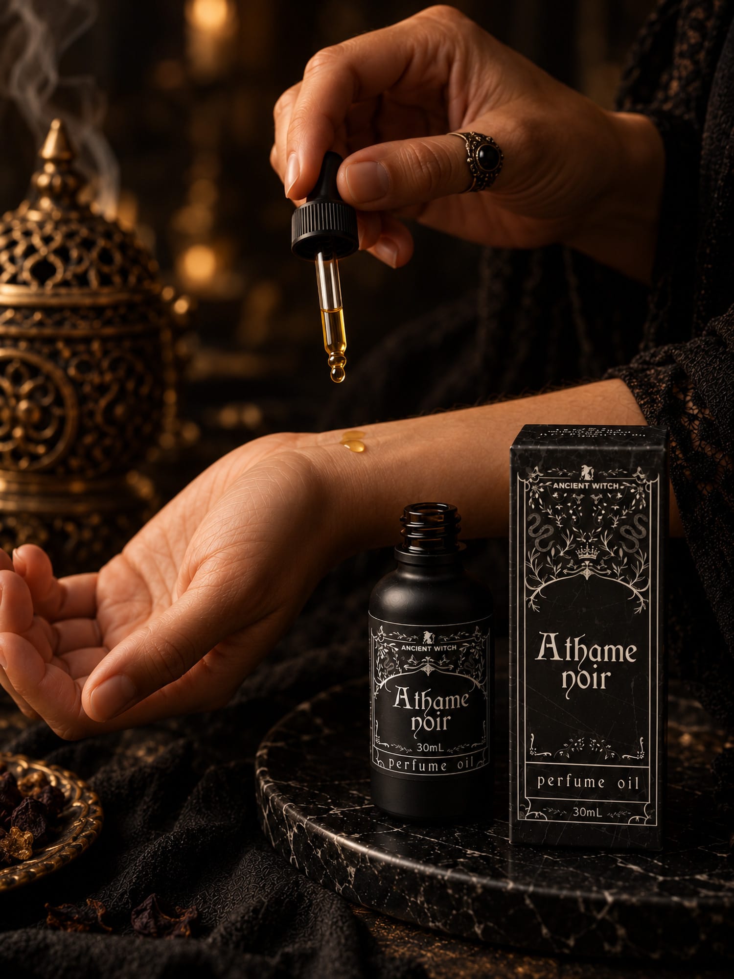 A drop of Athame Noir perfume oil being applied to a wrist beside the open 30ml bottle and presentation box.