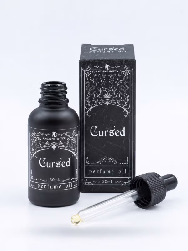 Open 30ml bottle of Cursed perfume oil with its glass dropper and black presentation box on a white background.